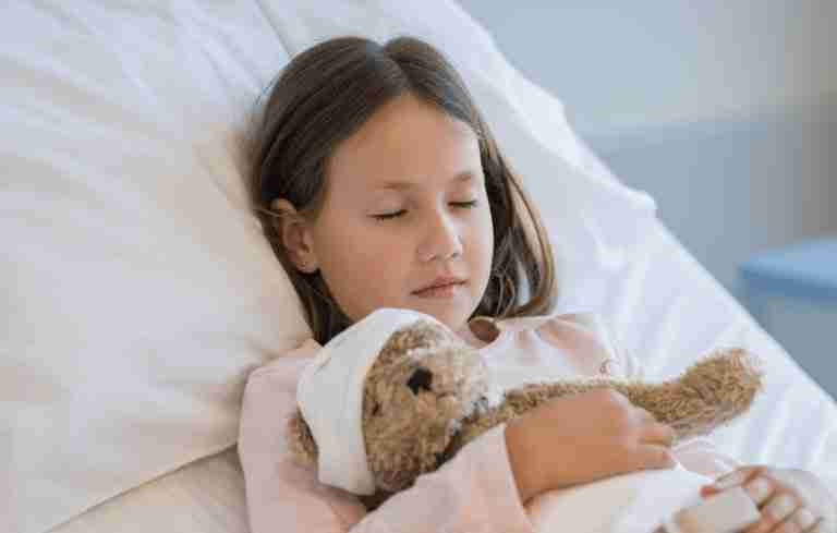 Child resting in bed with a teddy bear